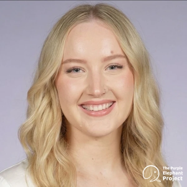 A woman with long blonde hair smiles at the camera against a light purple background. The Purple Elephant Project logo is in the bottom right-hand corner.