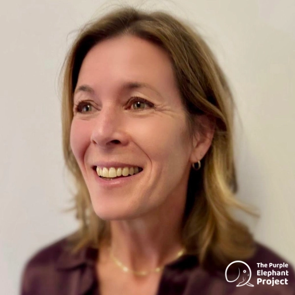 Smiling woman with shoulder-length brown hair facing left, wearing a dark top and hoop earring. The Purple Elephant Project logo is in the bottom right corner.