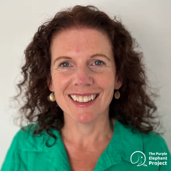 A woman with curly brown hair smiles at the camera, wearing a green top and gold earrings. The Purple Elephant Project logo is visible in the bottom right corner.