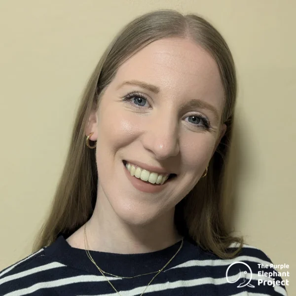 A woman with long, straight light brown hair smiles at the camera, wearing a striped top and gold jewellery. The Purple Elephant Project logo is in the lower right corner.
