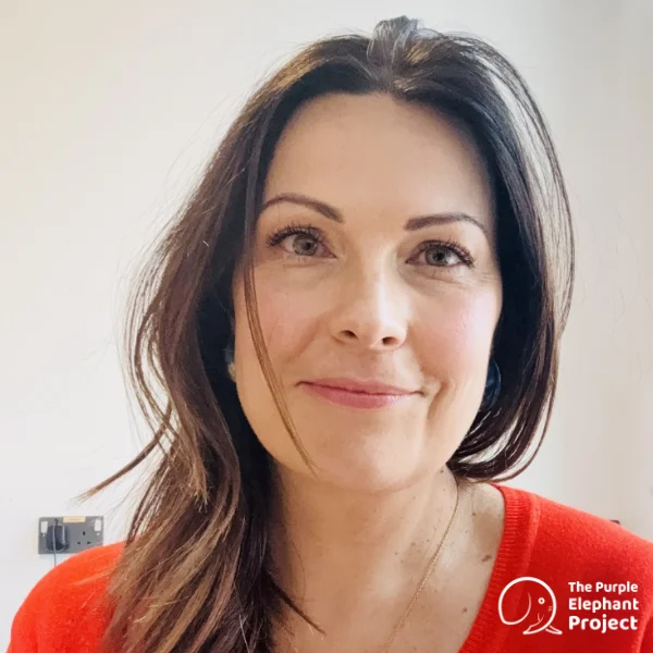 Gemma Kelly, with long brown hair wearing a red top, smiling softly at the camera. The Purple Elephant Project logo is in the bottom right-hand corner.