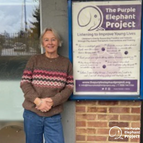 A person stands next to a sign for The Purple Elephant Project, an organisation focused on improving young lives, outside a building.
