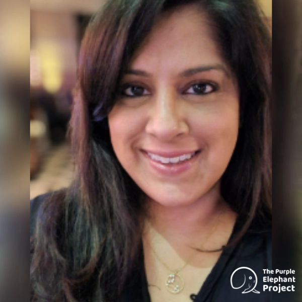A woman with long dark hair smiles at the camera. She is wearing a necklace, and the logo for The Purple Elephant Project appears in the bottom right-hand corner.