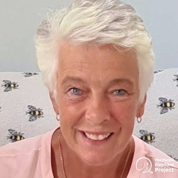Carlol, a woman with short white hair smiling at the camera, with a Purple Elephant Project logo in the bottom corner.