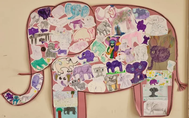 Large elephant outline on a wall, filled with various children’s elephant drawings in different styles and colours.
