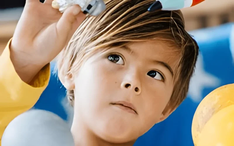 A young child in a yellow shirt holds up a toy astronaut and a toy rocket, looking at them with concentration. Blue and yellow decorations are visible in the background.